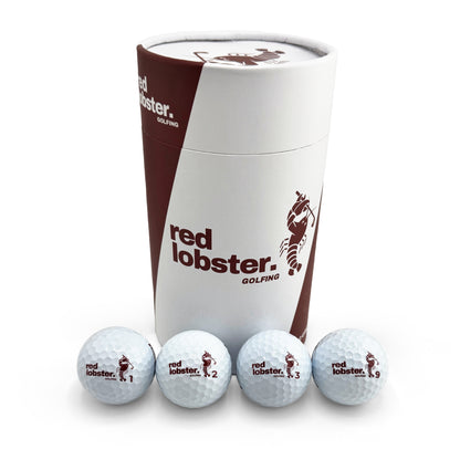 Vier weiße Lobbie PURE Golfbälle mit Red-Lobster-Golfing-Logo und den Nummern 1, 2, 3 und 9 vor der Geschenk-Tube